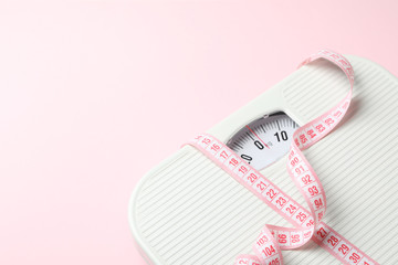 Scales and measuring tape on pink background. Weight loss concept