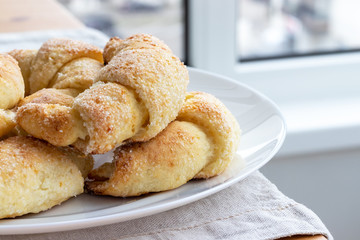 Sugar-frosted croissants from a cottage cheese dough on a white plate on a table with linen tablecloth. Tea snack for breakfast. The process of making curd bagels or croissants. Selective focus