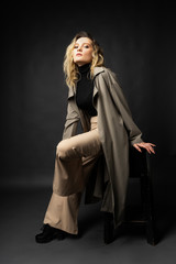 Beautiful girl wearing a casual trendy trousers, turtleneck and raincoat posing on a dark background. Fashionable, advertising, lifestyle and commercial design.