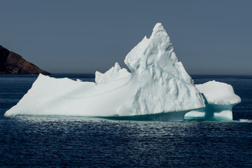 A large glacier iceberg with a high peak in the centre of the berg. The ocean is blue with small waves. The background is grey and foggy. 