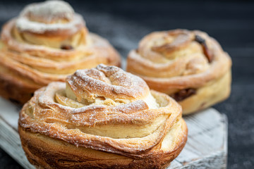 Bakery products with raisins and dried fruits are located on a dark wooden background. Sprinkled with icing sugar. Kraffins. Easter food.