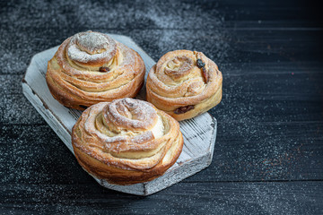 Bakery products with raisins and dried fruits are located on a dark wooden background. Sprinkled with icing sugar. Kraffins. Easter food.