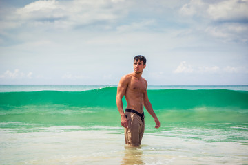 Fototapeta na wymiar Handsome young man standing on a beach in Phuket Island, Thailand, shirtless wearing boxer shorts, showing muscular fit body