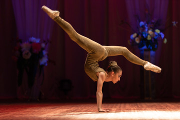 Young girl gymnast performs with a performance on stage in a theater