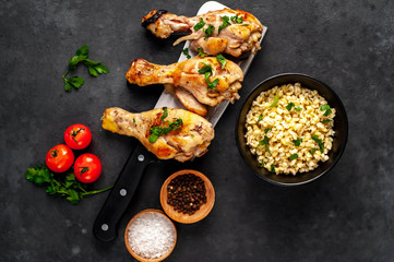Grilled chicken legs with spices on a knife and a bowl of cooked bulgur on a stone background with copy space for your text
