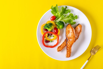 Salmon steak grilled with vegetables on yellow paper background. Healthy food concept.