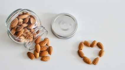 Almonds in a glass pot on a white table.  Almonds forming a heart shape. Concept of health.