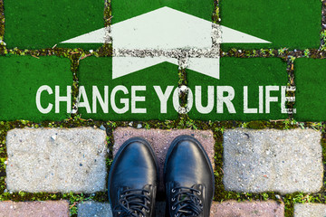 Zwei Schuhe vor einer grünen Fläche auf einem Gehweg mit dem weißen Text CHANGE YOUR LIFE