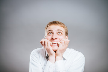 Closeup portrait of man biting his thumb fingernail or finger in mouth, very stressed and nervous, isolated on gray background with copy space