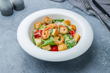 salad caesar with shrimps on white plate on grey table