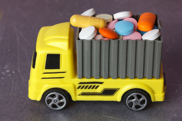 Transportation of medicines concept. A yellow toy truck delivering pills and drugs in a container