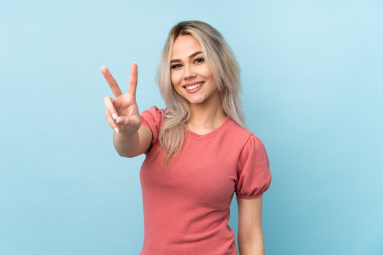 Teenager girl over isolated blue background smiling and showing victory sign