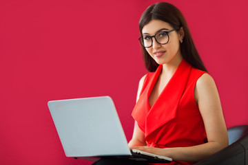 beautiful young woman with make-up in a red suit on a red background with a laptop
