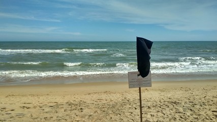 black flag on the beach against the backdrop of large storm waves. black lifeguard flag