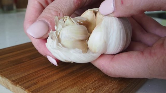 Anonymous female hands peeling garlic cloves on a wooden cutting board for increased immunity. Healthy food for fighting viruses. Concept of coronavirus or COVID-19 pandemic Slow motion Close up