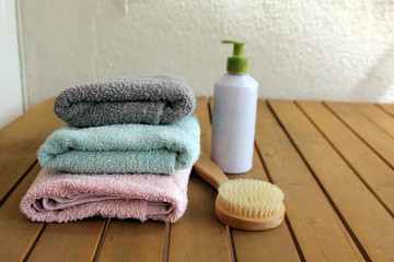 Obraz na płótnie Canvas pink, green and gray towels are lying on a wooden brown table on a white background next to a dry massage brush and body cream
