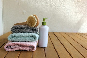 Obraz na płótnie Canvas pink, green and gray towels are lying on a wooden brown table on a white background next to a dry massage brush and body cream