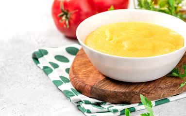 Traditional cooked polenta in a white bowl on a gray concrete table. Italian food.