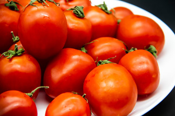 Ripe fresh red cherry tomatoes on a white plate against dark background.  Beautiful and healthy fresh cherry tomatoes without GMO.