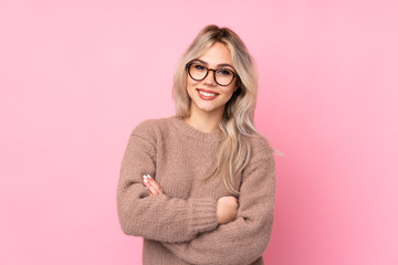 Teenager blonde girl wearing a sweater over isolated pink background with glasses and smiling
