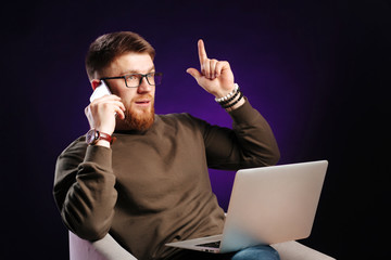 Handsome young bearded freelancer in casual clothes and glasses sitting at his working place and...