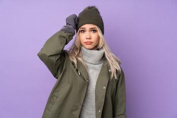 Teenager blonde girl with winter hat over isolated purple background with an expression of frustration and not understanding