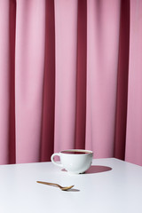 Cup of tea or coffee on white table in front of pink drapery, selective focus
