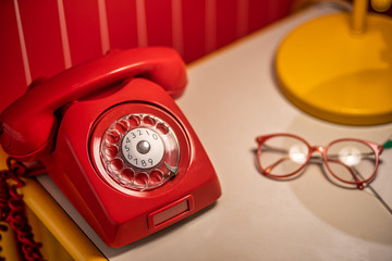 Old red telephone with rotary dial on the table with old glasses