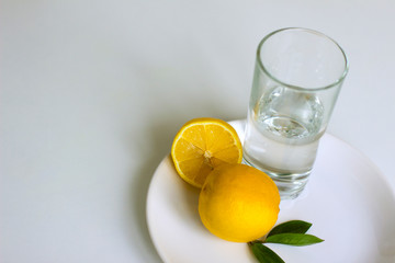 ripe yellow lemons and a refreshing glass of water on a white background
