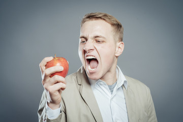 Cheerful beautiful man eating apple, isolated over gray background