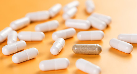 Fototapeta na wymiar Opposition. A lot of white pills and one brown on a yellow background. The problem of choice and efficiency. Health and medicine.