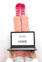 Stay home written on laptop screen. Legs up in pink socks on the white background