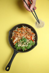 Udon noodles in a pan in a spicy sauce with pieces of chicken, sprouted mung bean and fresh herbs on a yellow background