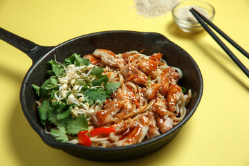 Udon noodles in a pan in a spicy sauce with pieces of chicken, sprouted mung bean and fresh herbs on a yellow background