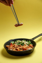 Udon noodles in a pan in a spicy sauce with pieces of chicken, sprouted mung bean and fresh herbs on a yellow background