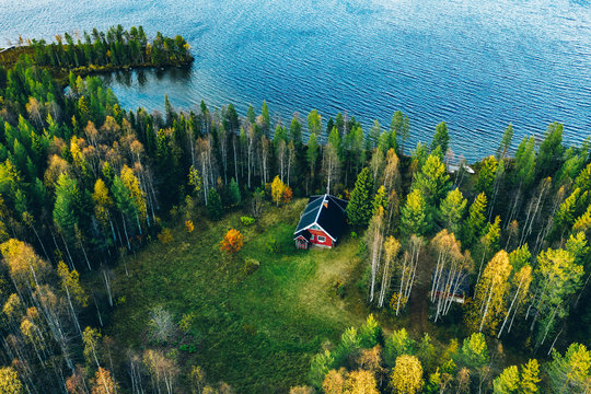 Aerial top view of red log cabin or cottage with sauna in spring forest by the lake in Finland