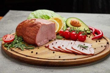 Sliced ham with spices, lettuce, avocado and tomatoes on wooden cutting board. Сold meat plate. Fresh prosciutto