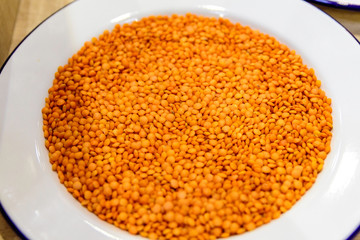 Top view of many orange red lentil beans on a white plate on a table, indoor background  with healthy vegan food photographed with selective focus

