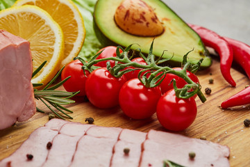 Fresh ripe tomatoes on a cutting board with ham, avocado, peper and lemon