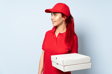 Pizza delivery girl holding a pizza over isolated background looking to the side and smiling