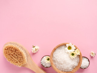 Spa flatlay composition. Sea salt in jars, massage wooden brush, flower on pink background. Copyspace, top view. Home care concept, relax and rest