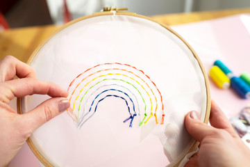 Hands of female sewing rainbow small embroidery pattern in wooden frame, colourful threads on...