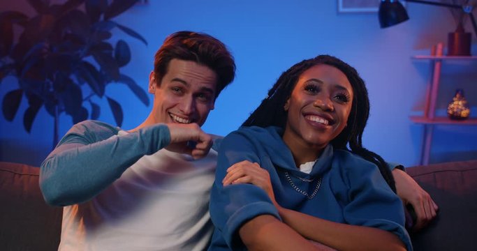 Millennial couple cuddling and laughing while spending time in front of tv. Young girl with dreadlocks and her lovely boyfriend watching comedy show at home.m Concept of leisure