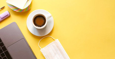 flat lay composition with laptop, pen, mask, coffee on yellow background. Concept remote study and work at home, telework, freelance, quarantine. Coffee break, office table. Copyspace, banner