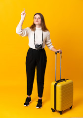 Full body of traveler teenager girl with suitcase over isolated yellow background touching on transparent screen