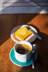 cup of hot fresh black coffee and a cake bread with sun light and shadow pattern on the wooden table 