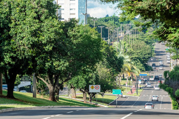 Low traffic of cars on a large avenue surrounded by big green trees of a wooded city. Photo taken at Afonso Pena avenue, Campo Grande - MS, Brazil.