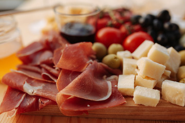 Cheese plate with prosciutto, tomatoes, grapes, olives, jam and honey on a wooden board.