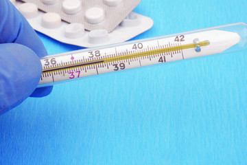 hand in medical gloves holding mercury thermometer showing fever temperature, copy space
