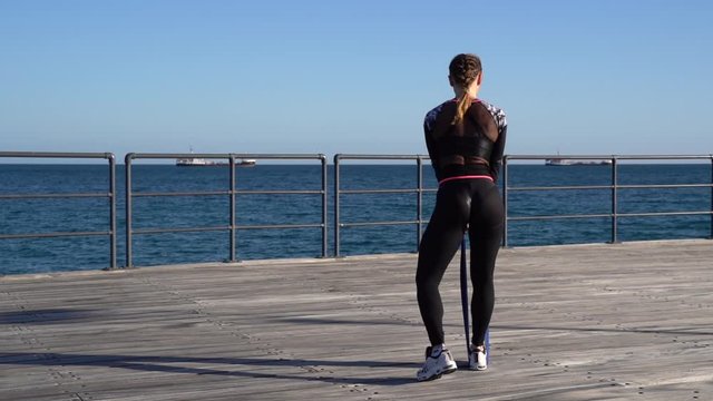 Caucasian female fitness model performing resistant band exercise outdoor at sea promenade